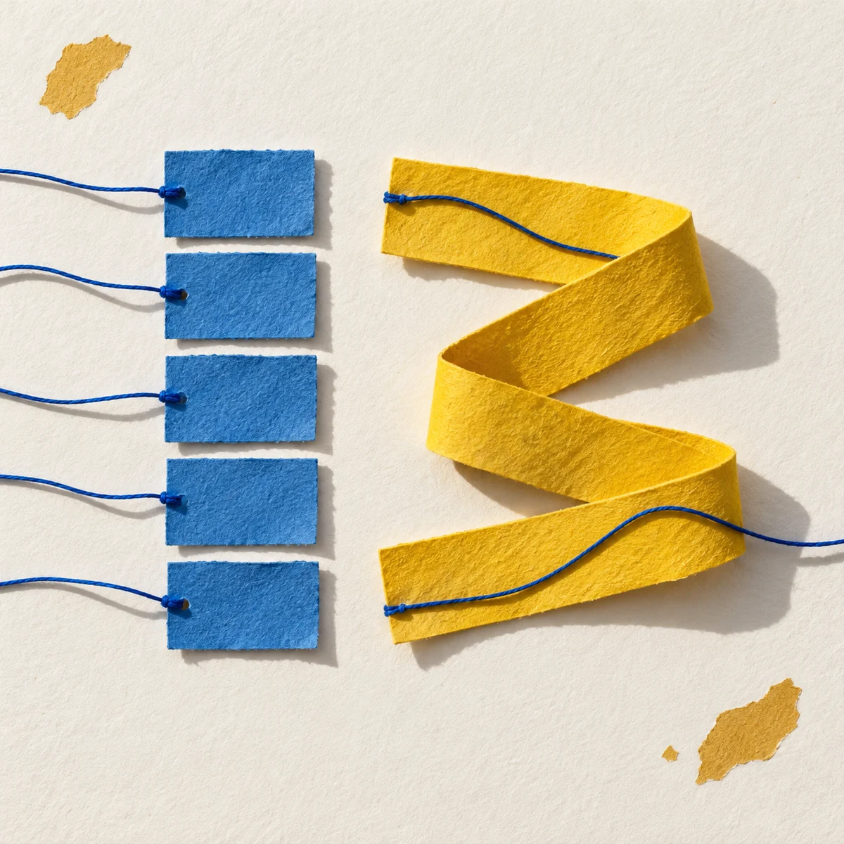 Separate blue paper pieces beside a continuous folded yellow strip, with blue threads connecting the paper shapes